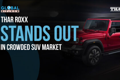 The image features a bold, eye-catching headline that reads "Thar Roxx Stands Out in Crowded SUV Market" set against a dark background. The visual showcases the new Mahindra Thar Roxx, a red five-door SUV, highlighted with sleek and modern design elements. The vehicle is positioned on the right side of the image, while the logo for "Global Biz Now" is displayed at the top left, emphasizing the focus on this new addition to the competitive SUV segment.